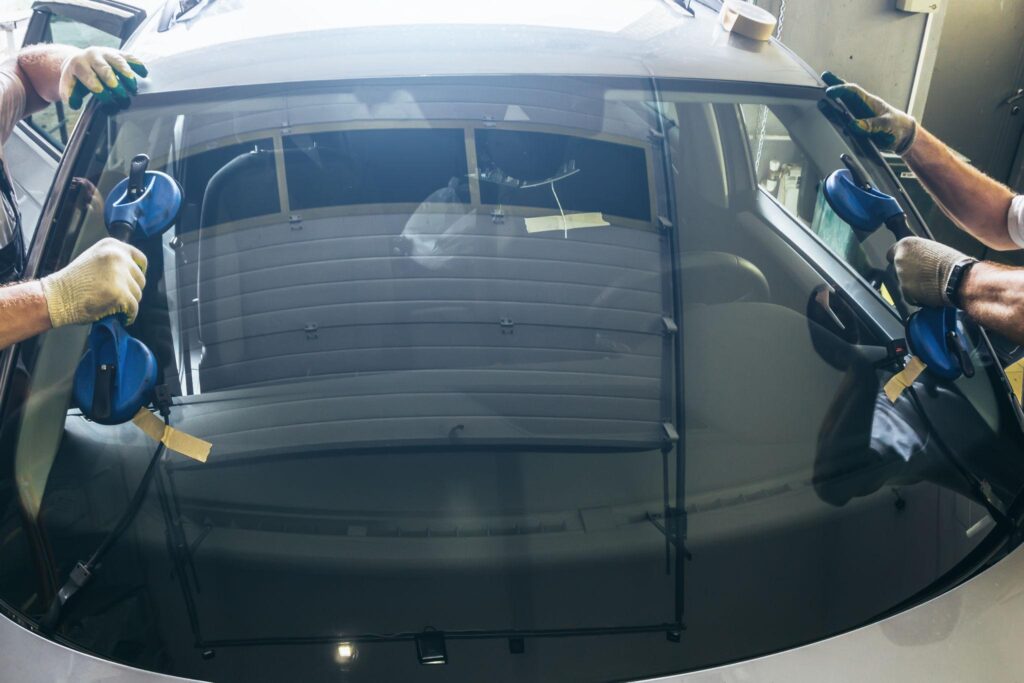 Technician installing a replacement windscreen on a vehicle in a professional auto glass workshop.