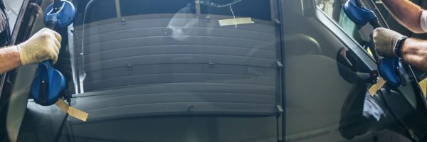 Technician installing a replacement windscreen on a vehicle in a professional auto glass workshop.